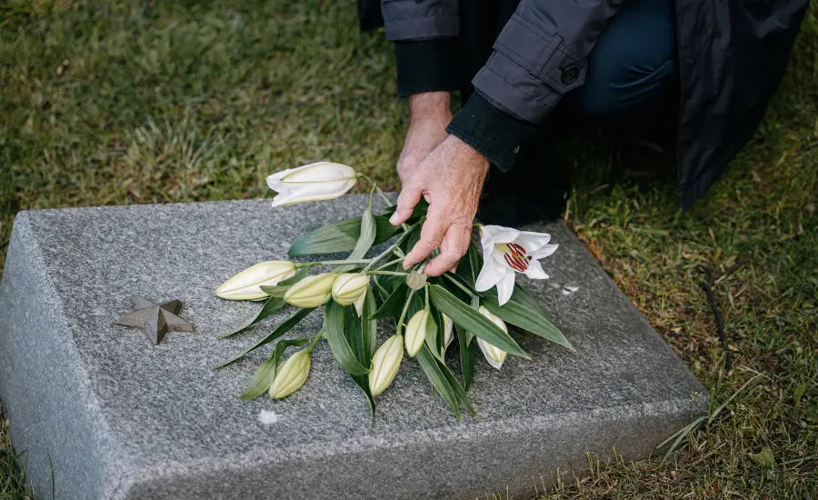 Manos colocando flores blancas sobre una lapida en senal de luto