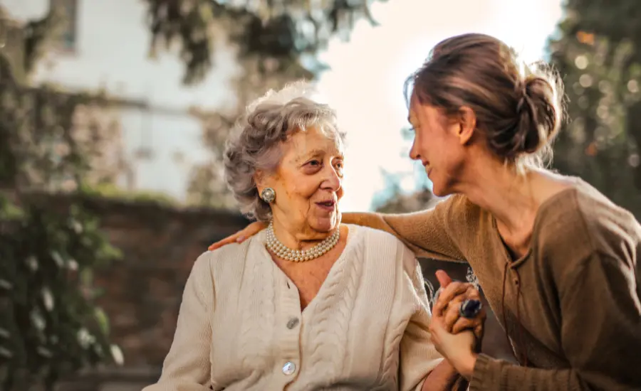 Madre mayor e hija adulta abrazadas sonriendo en jardin.